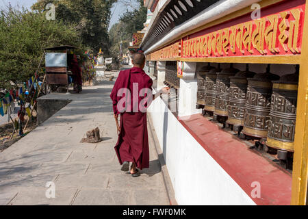 Nepal, Kathmandu, Swayambhunath. Junge buddhistische Mönch dreht Gebetsmühlen als er geht entlang der Mauer rund um den Stupa. Stockfoto