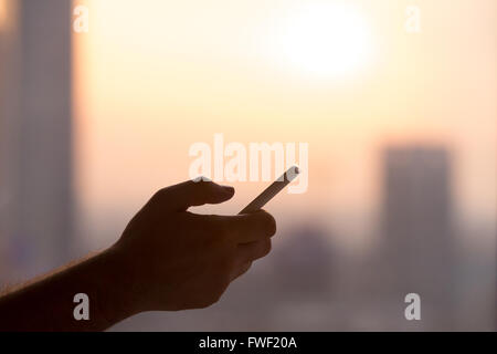 Nahaufnahme der Hände des Jünglings halten Handys, mit Smartphone-app scrollen. Silhouette gegen sonnigen Blick auf die Straße Stockfoto