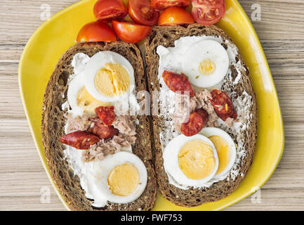 In Scheiben Vollkornbrot mit Butter, Thunfisch, Wurst, Cherry-Tomaten und Eiern auf dem Teller. Essen-Thema. Stockfoto