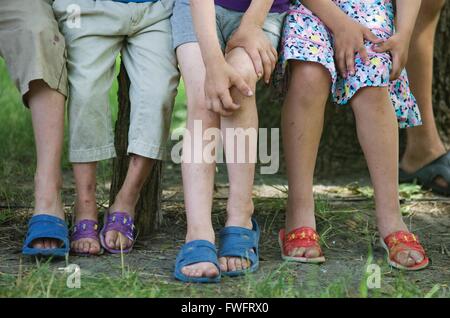 Odessa, Ukraine. Die Beine von Kindern wie sie auf einer Bank sitzen. Sie können nicht sehen, die Kinder-Gesichter, aber die Kinder tragen bunte Flip-Flops und Sandalen, aber ihre Beine sind dünn und gequetscht. Ihre Kleider sind alt und schmutzig, und sie sind arm. Stockfoto