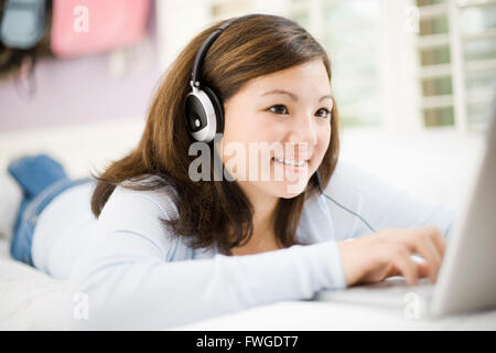 Ein Mädchen liegt auf ihrem Bett mit Kopfhörern, mit einem Laptopcomputer. Stockfoto