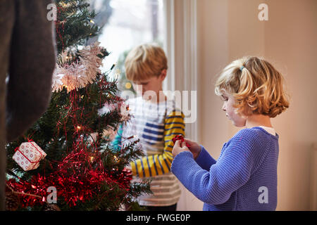 Zwei Kinder schmücken Weihnachtsbaum in einem Einfamilienhaus. Stockfoto