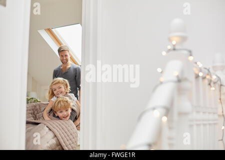 Zwei Kinder und ein Mann in einem Schlafzimmer schauen aufgeregt durch die Tür. Stockfoto