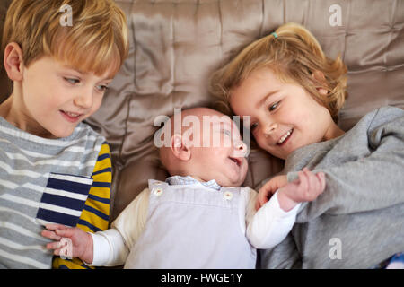 Drei Kinder auf einem Bett, einem jungen und Mädchen mit einem Baby zwischen ihnen liegen. Stockfoto