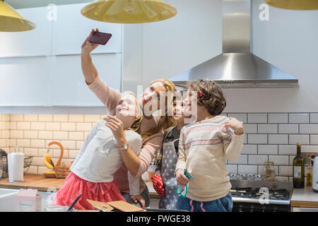 Eine erwachsene Frau und drei Kinder mit dem selfy Fotografieren in der Küche. Stockfoto