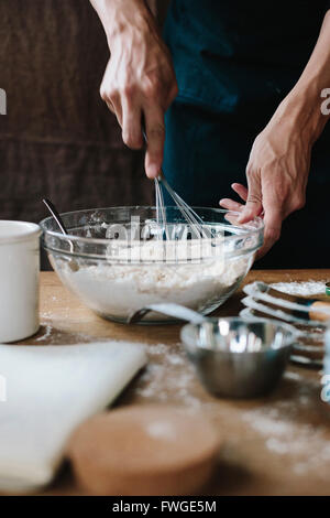Eine Person mit einem Schneebesen mischen Zutaten in einer Schüssel auf einem Küchentisch. Stockfoto