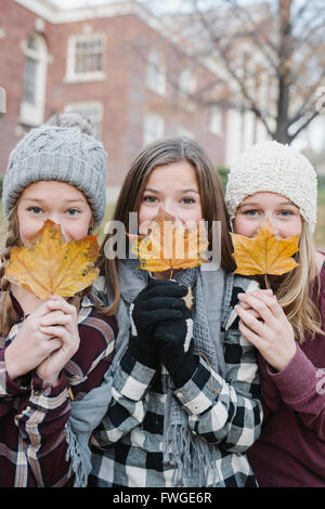Drei junge Mädchen in einer Zeile stehen, verlässt Herbst halten vor den Gesichtern. Stockfoto
