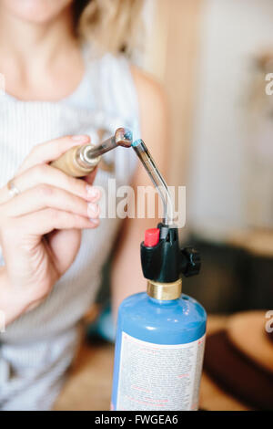 Eine Frau hält eine Hand-Werkzeug in die Flamme einer Lötlampe Metall Heizung. Stockfoto