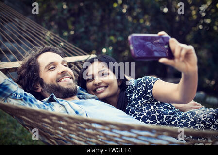 Ein paar, ein junger Mann und Frau, die große Hängematte im Garten, die eine selfy von sich selbst. Stockfoto