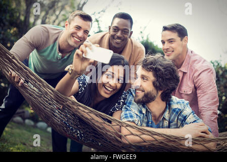 Eine Gruppe von Freunden Faulenzen in einer großen Hängematte im Garten ein Bier, und ein Selbstporträt. Stockfoto