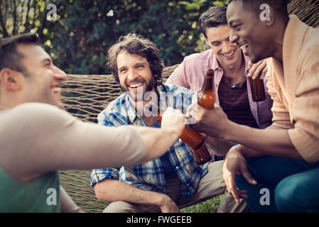 Eine Gruppe von Freunden in einer großen Hängematte im Garten mit einem Bier entspannen. Stockfoto