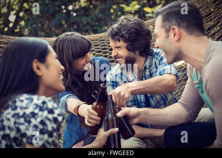 Eine Gruppe von Freunden in einer großen Hängematte im Garten mit einem Bier entspannen. Stockfoto