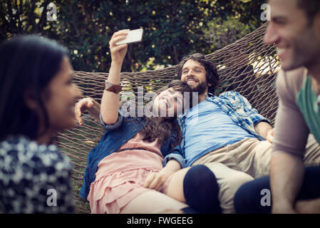 Eine Gruppe von Freunden Faulenzen in einer großen Hängematte im Garten ein Bier, und ein Selbstporträt. Stockfoto