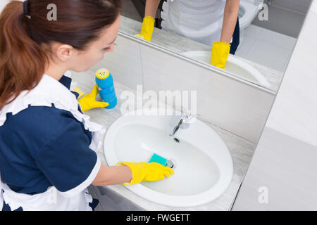 Vogelperspektive Blick auf Haushälterin mit gelben Gummihandschuhen Waschbecken mit blauen Schwamm reinigen und schrubben Pulver Stockfoto
