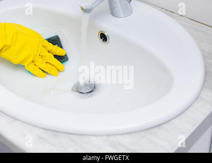 Detail-Ansicht auf der Seite mit gelben Gummihandschuh Spülbecken mit blauen Schwamm abwischen und fließendem Wasser bedeckt hautnah Stockfoto