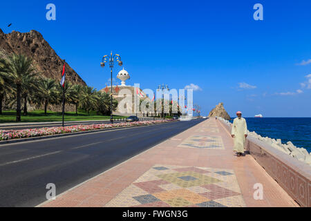 Mann trägt Dishdasha Spaziergänge Mutrah Corniche mit Nationalflaggen, Blumenbeeten und riesigen Weihrauch-Brenner, Muscat, Oman Stockfoto