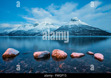 Blauer Himmel in der Dämmerung und schneebedeckte Gipfel spiegeln sich in das gefrorene Meer, Storfjorden, Lappland, Lyngen Alpen, Troms, Norwegen, Skandinavien Stockfoto