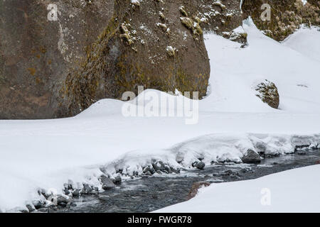 Schmalen Bach zwischen Felsen, umgeben von Schnee.  Winter in Thorsmork, Island Stockfoto