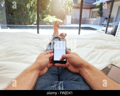 Nahaufnahme Bild des Mannes liegen auf einem Bett, ein Mobiltelefon mit leeren Bildschirm halten. POV Aufnahme von entspannenden Mann im Schlafzimmer mit Touch sc Stockfoto