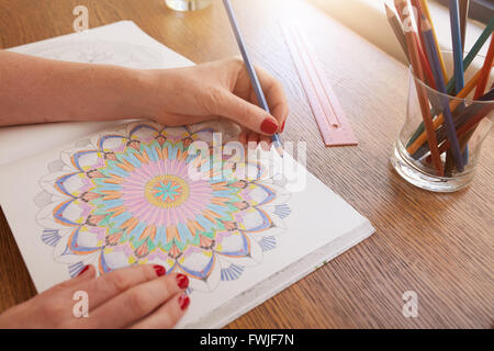 Schließen Sie herauf Bild der Frau Hände zeichnen in Erwachsene Malbuch auf einem Tisch zu Hause. Stockfoto