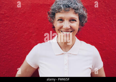 Porträt des Lächelns Reife Frau vor rotem Hintergrund hautnah. Applying Frau mit schönen Lächeln. Stockfoto