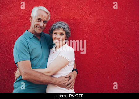 Porträt des Liebens Mitte im Alter von Mann und Frau stehen gemeinsam vor rotem Hintergrund. Älteres paar umarmt gegen rote Wand Stockfoto