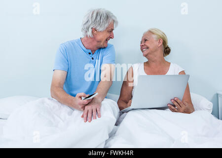 Fröhliche Ehepaar im Ruhestand mit Laptop auf dem Bett sitzend Stockfoto