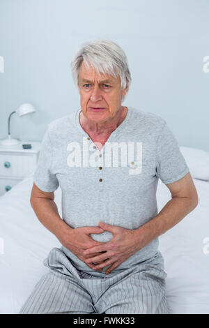 Ältere Mann berühren Magen sitzend auf Bett Stockfoto