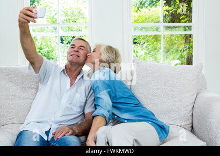 Ältere Frau küssen während der Mann unter Selfie im Wohnzimmer Stockfoto