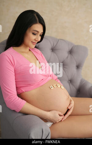 Porträt einer schwangeren Frau mit Buchstaben auf den Bauch Stockfoto