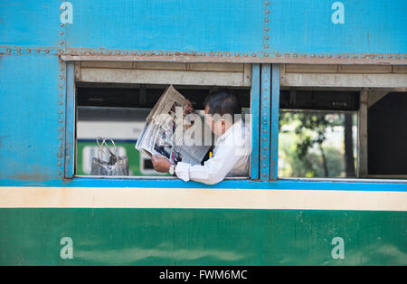 Mann liest die Zeitung auf der kreisförmigen Bahn, Yangon, Myanmar Stockfoto