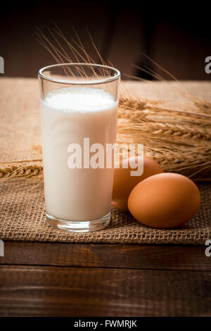 Glas Milch, Eier und Weizen Ohren liegen auf der Serviette aus Sackleinen auf dem alten Holztisch Stockfoto