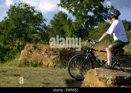 Radfahrer auf Schinken-Hügel, Somerset, England, ruht Menschen junger Mann ruht auf Felsen trinken Getränke aus Wasserflasche sitzen Fahrrad Stockfoto