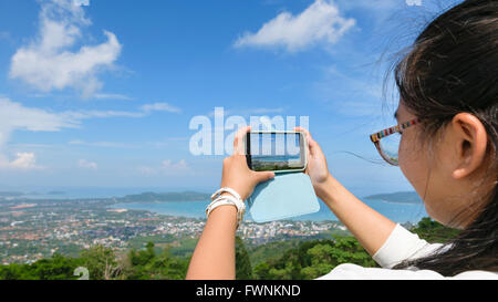 Junge Frauen Touristen fotografieren erhöhte Ansicht von Ao Chalong Bucht und die Stadt Meerseite mit Mobiltelefonen auf Yot Khao Nak Ke Stockfoto