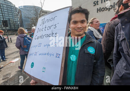 London, UK. 6. April 2016. Ein Mann in grün chirurgische Peelings steht vor dem Eingang, St Thomas' Hosptial mit ein großes Plakat bleiben, dass die Junior Ärzte neue Verträge mit Jerremy Hunt will verhängen sind unsicher, unfair, sexistische und unwissenschaftlich. Peter Marshall/Alamy Live-Nachrichten Stockfoto