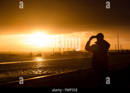 Gravesend, Kent. 7. April 2016. Ein Mann fotografiert Sonnenaufgang auf der Themse, hinter Schiffe in Gravesend, Kent heute Morgen gesehen. Eine Mischung aus Regen und Sonnenschein Prognose für das Wetter in London und der Südosten von England heute. Bildnachweis: Versand Bilder/Alamy Live News Stockfoto