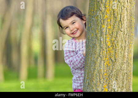 Kleines Mädchen versteckt sich hinter einem Baum in einem Wald Stockfoto