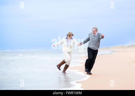 Mittleren Alter Brautpaar laufen am Strand Hand in Hand und springen weg von den Wellen Stockfoto