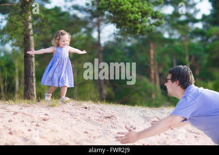 Lockige glücklich Mädchen spielen mit ihrem Vater, ausgeführt von einer Sanddüne in einem Pinienwald auf einem sonnigen, warmen Sommertag Stockfoto