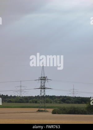 Drei Säulen der Hochspannungsleitungen in Mecklenburg-Vorpommern, Deutschland. Sonnenstrahlen sind auf den bewölkten Himmel sichtbar. Stockfoto