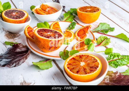 Blutorangen auf weißen Tellern mit grünem Salat Blätter Stockfoto