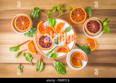 Blutorangen auf weißen Tellern mit grünem Salat Blätter auf Holz, Ansicht von oben Stockfoto