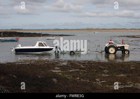 Zwei Männer bereiten ein kleines Fischerboot aus dem Meer auf einem Start Wagen abgeschleppt von einem weißen David Brown Traktor getroffen werden. Stockfoto