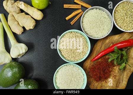 Vier Schalen mit verschiedenen Arten von Reis: Wildreis, weiß, Basmati-Reis, brauner Reis und indische Gewürze auf Oliven-Holzplatte und b Stockfoto