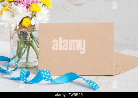 Frühling Blumen Blumenstrauß in einer Glas-Vase mit Kraft Karte Hinweis, Umschlag und blaue gepunktete Band auf weißem Holz rustikal Hintergrund Stockfoto