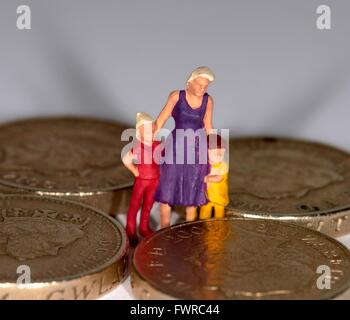 Eine Miniatur Figur Frau mit 2 Kindern steht zwischen einem Pfund-Münzen Stockfoto