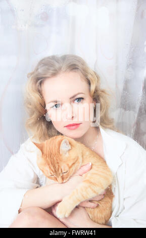 Schöne Frau am Fenster mit einer roten Katze an ihren Händen Stockfoto