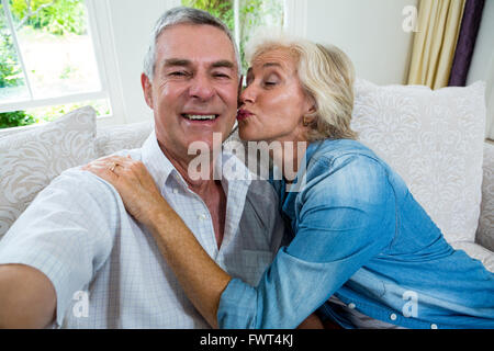 Ältere Frau küssen Mann beim Sitzen auf einem Sofa begeistert Stockfoto