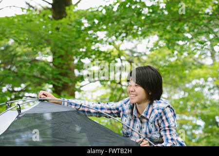 Junge japanische Frau, die ein Zelt auf einem Campingplatz aufstellen Stockfoto