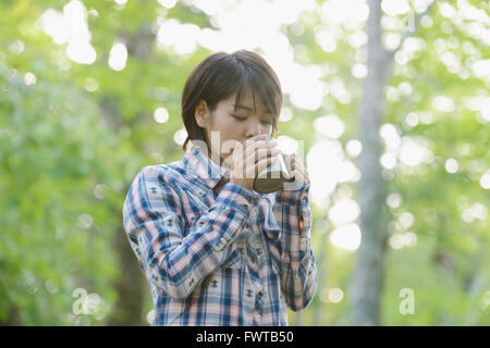 Junge Japanerin Kaffeetrinken auf einem Campingplatz Stockfoto